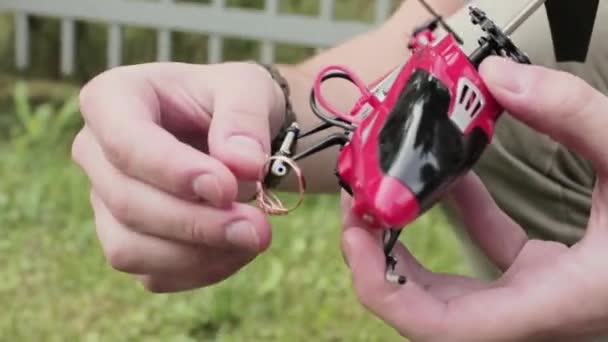 Guys hand holds red nano toy helicopter and puts wedding ring on its skids - Footage, Video