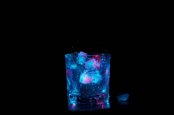 Siyah bir arka plan üzerinde izole mavi ve kırmızı ışıklar altında berrak sıvı dolu bir kaya cam içine sıçramasına buz - Fotoğraf, Görsel