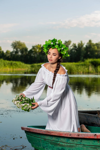 Young sexy woman on boat at sunset. The girl has a flower wreath on her head, relaxing and sailing on river. Fantasy art photography. - Фото, зображення