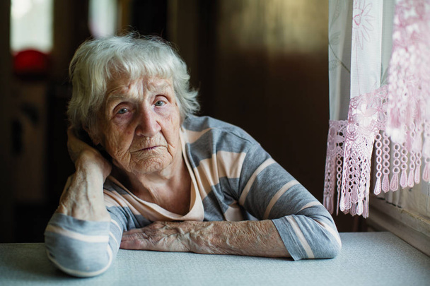 Una anciana pensionista se sienta tristemente cerca de la ventana
. - Foto, imagen