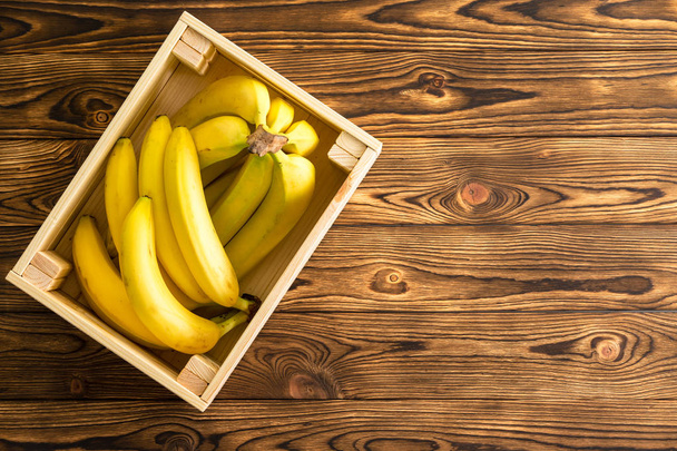 Large light colored rectangular wooden box holding two groups of yellow bananas over flat wood grain background - Valokuva, kuva
