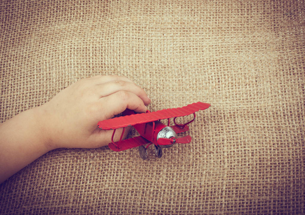 Mão segurando um avião de brinquedo vermelho em uma tela de linho
 - Foto, Imagem