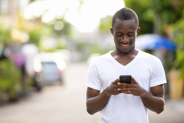 Joven hombre africano feliz sonriendo mientras usa el teléfono en las calles al aire libre
 - Foto, imagen
