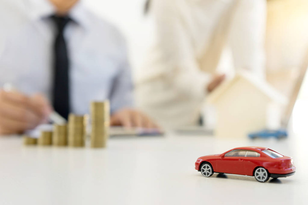 молодий бізнесмен працює за столом стоїть монети в офісі фокус на моделі червоного автомобіля
 - Фото, зображення