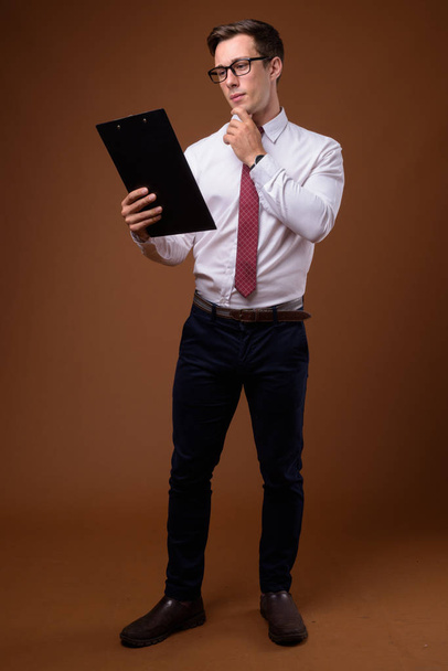 Jonge knappe zakenman dragen van bril tegen bruine rug - Foto, afbeelding