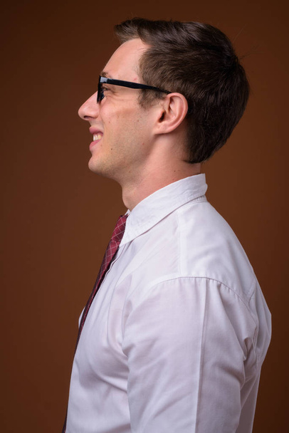 Jonge knappe zakenman dragen van bril tegen bruine rug - Foto, afbeelding