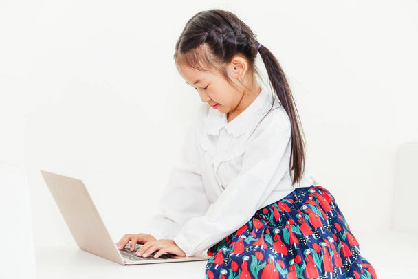 Um miúdo feliz a usar um computador portátil sentado no sofá branco. Estilo de vida infantil
. - Foto, Imagem