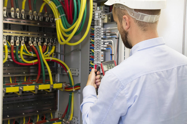 Electrician engineer at work inspecting cabling connection of high voltage power electric line in industrial distribution fuseboard. Service man with multimeter - Foto, Imagen