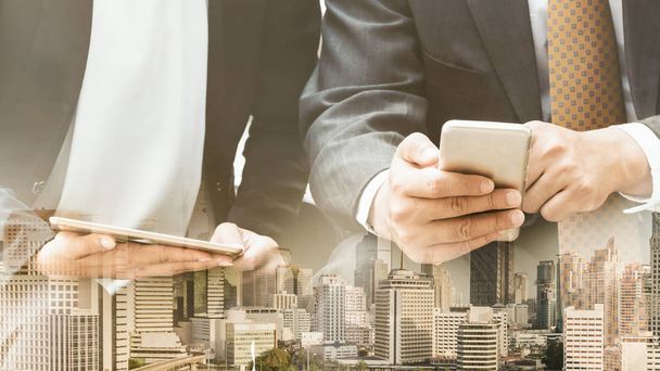 Молодые бизнесмены пользуются мобильным телефоном на фоне современных городских зданий. Концепция будущего телекоммуникационных технологий и интернета вещей (IOT)
. - Фото, изображение