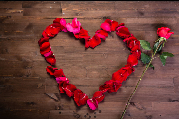 Auf dem Holztisch liegen eine rosa Rose und ein Herz aus Rosenblättern. der mittlere Plan - Foto, Bild