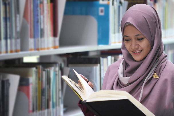 Młody student hidżabu czytający książkę w bibliotece publicznej. - Zdjęcie, obraz