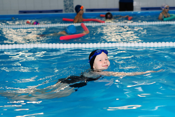 Zwemles voor kinderen in het zwembad - mooi fair-gevild meisje zwemt in het water - Foto, afbeelding
