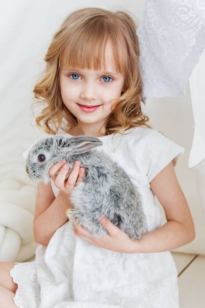 Cute girl hugging with rabbit while sitting on the floor at home - Foto, Imagen