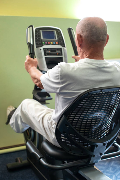 Ein sehr alter Mann sitzt im Fitnessstudio im Simulator - Foto, Bild