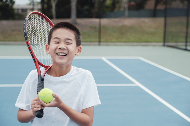 Young tween Asian boy tennis player on outdoor blue court - 写真・画像