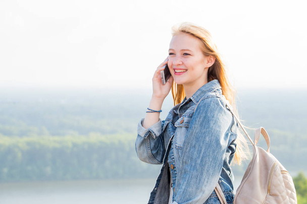 Young happy student girl talking on smartphone and smiling on nature background - 写真・画像