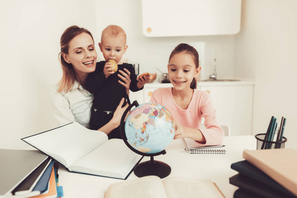 Mom Helps Daughter To Do Homework In The Kitchen. Family Relationship Concept. Educational Childhood. Studying At Home. Knowledge Receiving. Hold A Baby. Parents Duty. Working Together. - 写真・画像