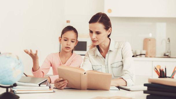 Mom Helps Daughter To Do Homework In The Kitchen. Family Relationship Concept. Educational Childhood. Studying At Home. Knowledge Receiving. Information Writing. Parents Duty. Working Together. - Photo, Image
