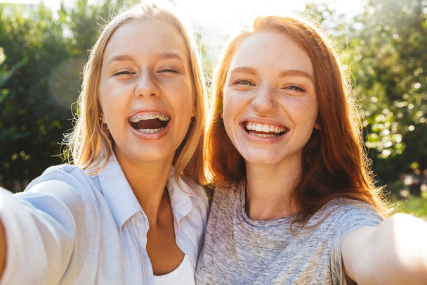 Two cheerful youg girls having fun at the park, taking a selfie - Foto, afbeelding
