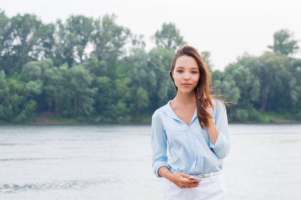 Horizontal portrait of a beautiful attractive woman on the waterfront background. Young girl looking at camera and smiling. copy space. - 写真・画像