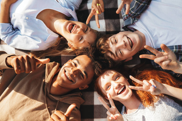 Image of happy young friends men and women laughing and lying on blanket in circle - Φωτογραφία, εικόνα
