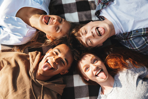 Image of stylish friends men and women laughing and lying on blanket in circle outdoor - Фото, зображення