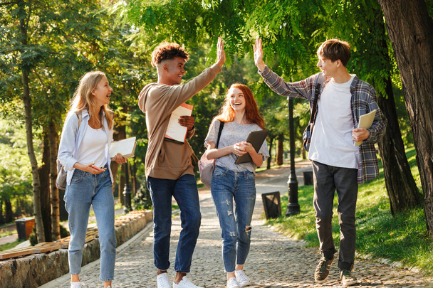 Group of laughing students walking at the campus outdoors, giving high five - Fotoğraf, Görsel