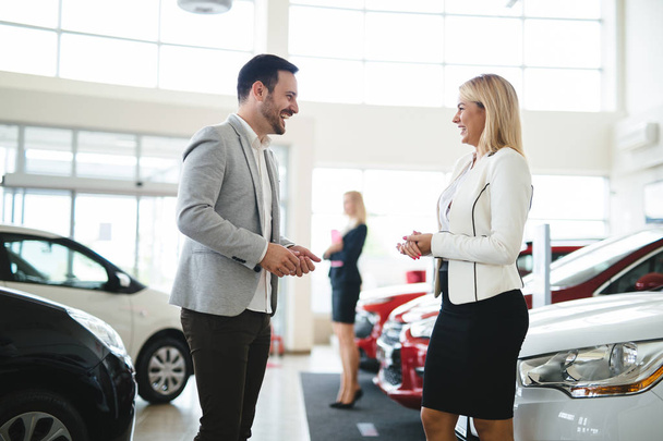 Woman is talking to handsome car dealership worker while choosing a car in dealership - Fotoğraf, Görsel