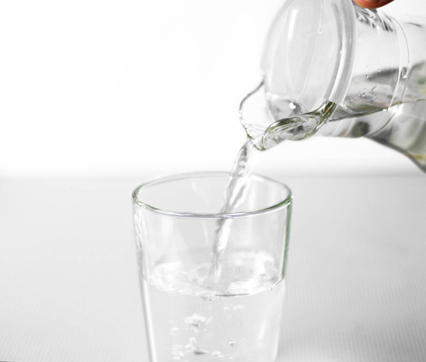 Hand pours water into a glass glass Cup from a glass jug. Close up. Isolated on white background - Photo, Image