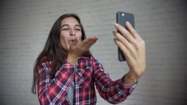 Fun portrait of laughing attractive young woman with phone gesture in hand laughing at camera, on grey background - Video, Çekim