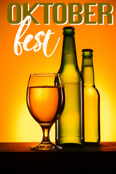 bottles and glass of beer on surface on orange background with "oktoberfest" lettering - Фото, изображение