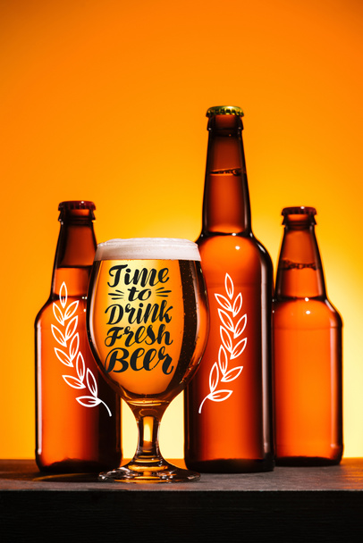 bottles and glass of beer with foam on surface on orange background with "time to drink fresh beer" inspiration - Photo, Image