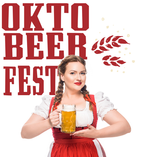 attractive waitress in traditional bavarian dress holding mug of light beer isolated on white background with "oktoberfest" lettering - 写真・画像