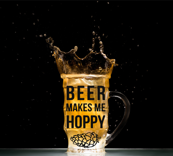 Glas helles Bier mit Spritzern am Tisch auf schwarzem Hintergrund mit dem Schriftzug "Bier macht mich moppig" - Foto, Bild