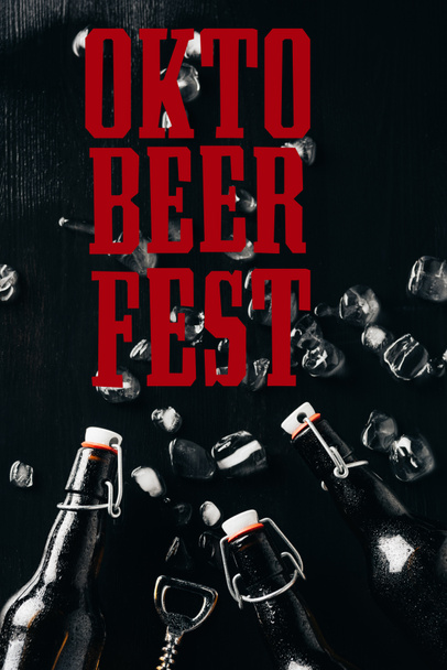acostado plano con abridor de botellas, botellas de vidrio de cerveza y cubitos de hielo dispuestos en la mesa oscura con letras "oktoberfest"
 - Foto, imagen