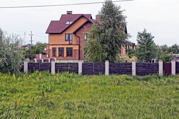 великий приватний будинок з вікнами за дерев'яним парканом з воротами в зеленій рослинності на вулиці
 - Фото, зображення
