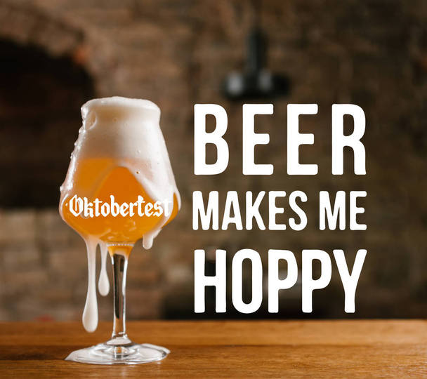 close-up view of cold beer with foam in glass on wooden table with "oktoberfest - beer makes me hoppy" inspiration - Фото, зображення