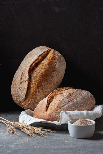 close up view of loafs of ciabatta and wheat on black background - Foto, Imagem
