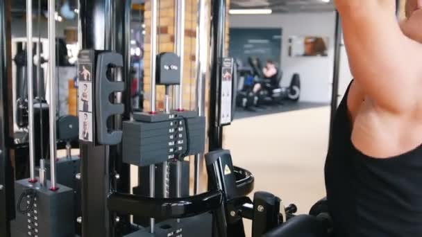 Bodybuilder in a black tank top performs an exercise on shoulder pull down machines - Filmagem, Vídeo