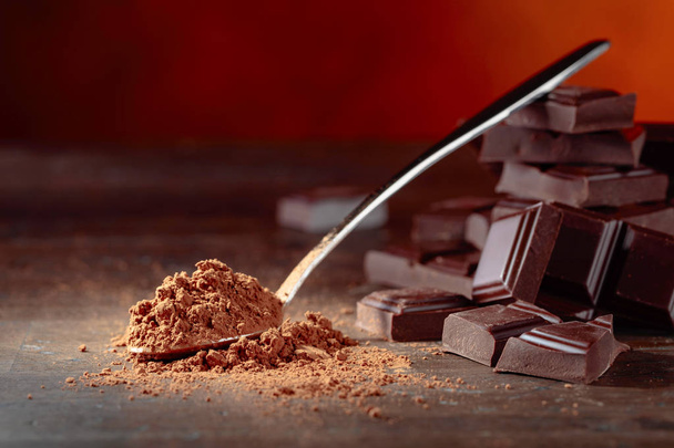 Schokoladenstücke und Kakaopulver in einem kleinen Löffel auf einem alten Holztisch. - Foto, Bild
