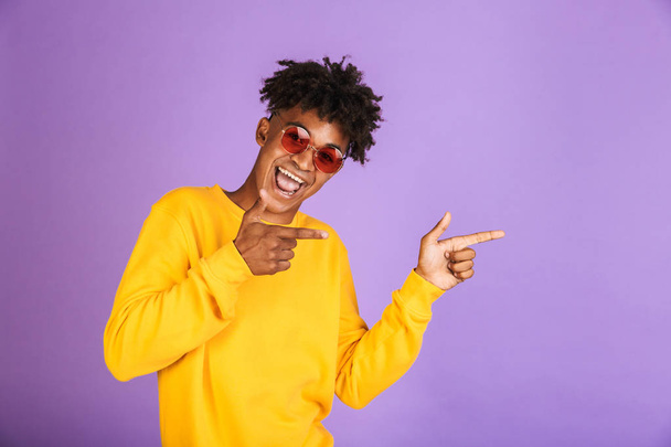 Portrait of a happy young afro american man in sweatshirt isolated, pointing away at copy space - Фото, зображення