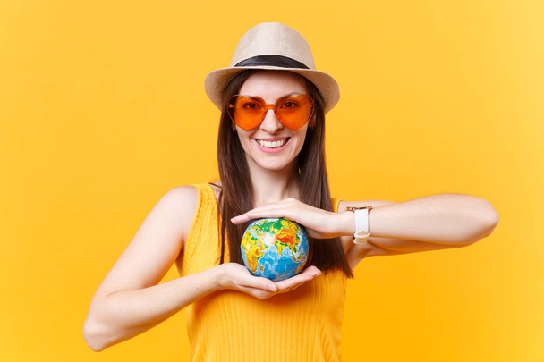 Portret kobiety turystycznych w letni kapelusz, okulary pomarańczowy trzymać w ręce globu na białym tle na żółtym tle. Pobytu za granicą, podróż weekendy wypad. Powietrze lot podróż koncepcja. Zatrzymać śmieci natura - Zdjęcie, obraz