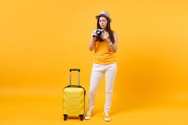 Туристична жінка в літньому повсякденному одязі з валізою, ретро вінтажна фотокамера ізольована на жовтому помаранчевому фоні. Пасажири, які виїжджають за кордон у відпустку у вихідні дні. Концепція авіарейсу
 - Фото, зображення