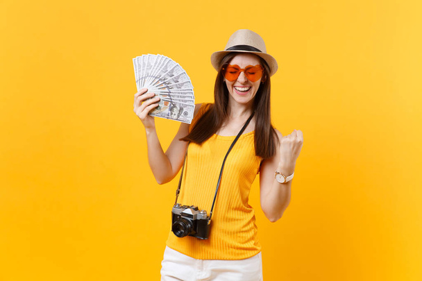 Mulher turística em roupas casuais de verão, chapéu segurando lotes de dólares, dinheiro em dinheiro isolado no fundo laranja amarelo. Mulher viajando para o exterior para viajar nos fins de semana de fuga. Conceito de voo aéreo
 - Foto, Imagem