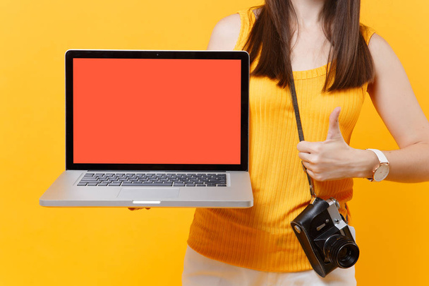 Обрізана туристична жінка тримає комп'ютер ноутбука з порожнім чорним порожнім екраном ізольовано на жовтому помаранчевому фоні. Жінка, яка виїжджає за кордон, щоб подорожувати у вихідні дні. Концепція авіаперельоту
 - Фото, зображення