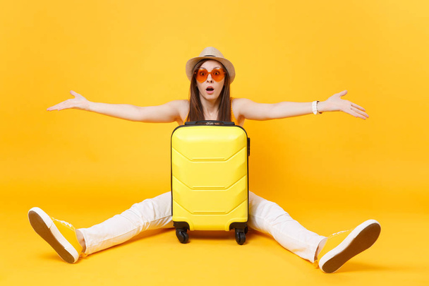 Mujer turista viajero triste en ropa casual de verano, sombrero se sienta cerca de la maleta aislado sobre fondo amarillo naranja. Pasajera viajando al extranjero para viajar los fines de semana. Concepto de vuelo aéreo
 - Foto, imagen