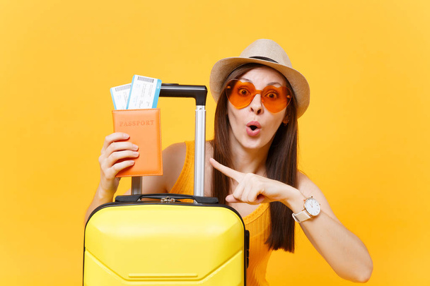 Femme touristique amusante en vêtements décontractés d'été, chapeau, lunettes de soleil orange avec valise, passeport isolé sur fond jaune. Passager voyageant à l'étranger pour voyager le week-end escapade. Concept de vol aérien
 - Photo, image