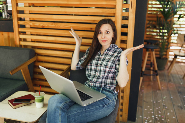 Сумна дівчина на вулиці літня кав'ярня дерев'яна кав'ярня, що сидить у повсякденному одязі, працює на сучасному комп'ютері для ноутбуків, у вільний час. Мобільний офіс. Концепція вільного бізнесу способу життя
 - Фото, зображення