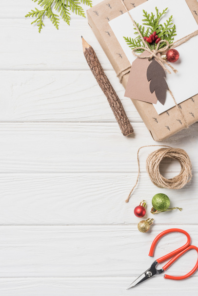 Draufsicht auf dekoriertes Weihnachtsgeschenk mit Kugeln in der Nähe von Bleistift und Schere auf Holztisch - Foto, Bild