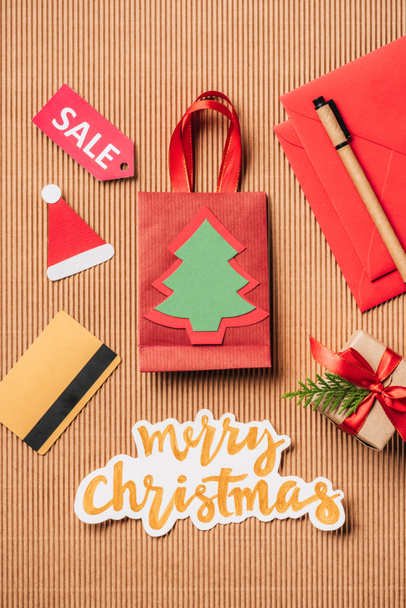 top view of red shopping bag, decorated gift box, credit card and merry christmas lettering on surface  - Foto, immagini
